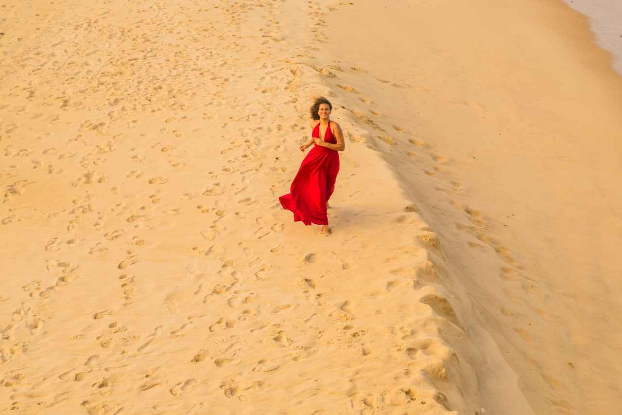 Ensaio feminino na Praia de Arembepe, Bahia, com vestido vermelho esvoaçante. A imagem simboliza liberdade e movimento, explorando a luz suave e o cenário natural da praia. Um registro perfeito para quem busca um ensaio com energia, cor e emoção.