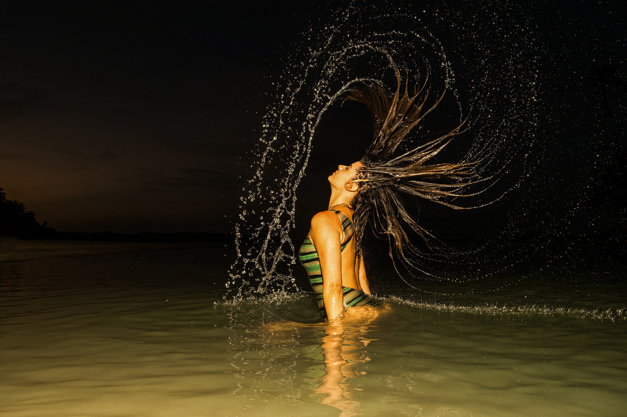 Ensaio feminino em Boipeba, Bahia, com movimento de água e iluminação criativa. A imagem simboliza poder e autenticidade feminina, destacando o contraste entre o escuro do mar e o brilho da pele.