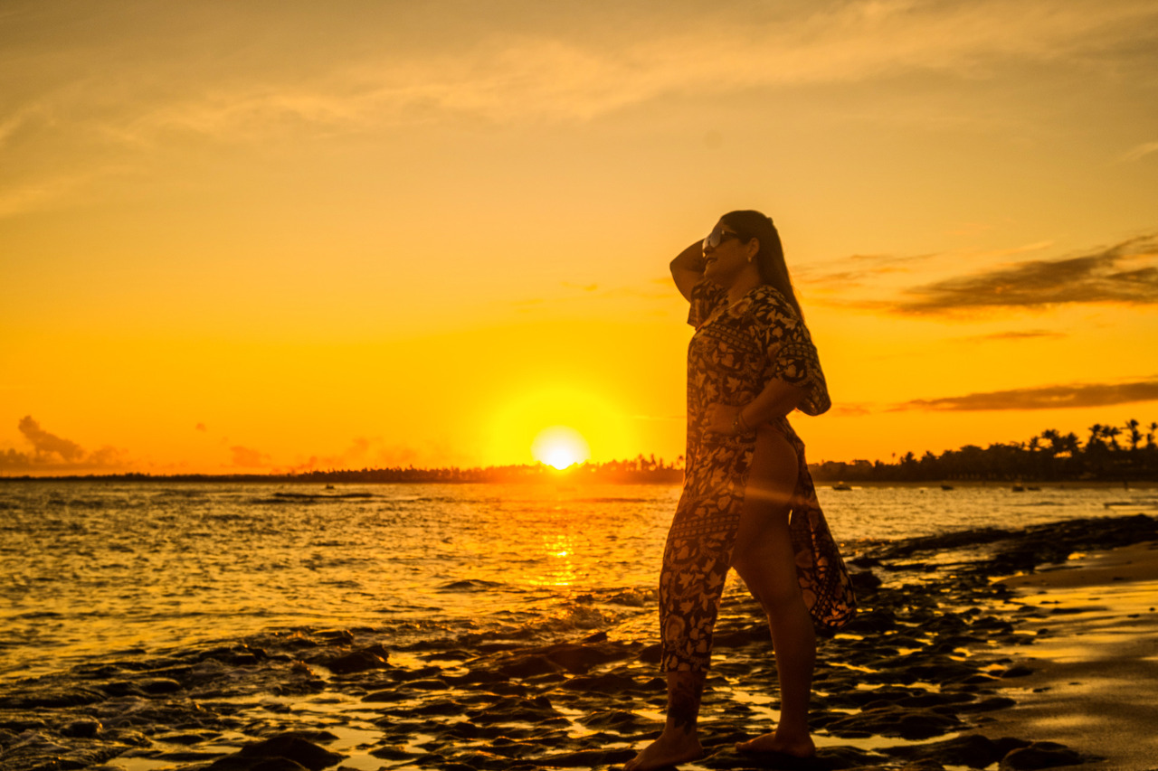 Fotografia feminina ao pôr do sol na Praia do Forte, Bahia. A cena combina luz dourada, mar calmo e o charme tropical do destino. Ideal para quem deseja eternizar momentos de conexão com a natureza em um ensaio fotográfico profissional.
