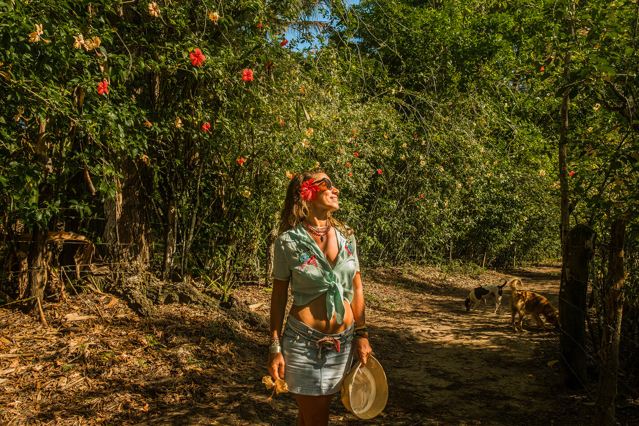 Mulher caminhando pela Trilha dos Hibiscus em Bainema, Boipeba, cercada por vegetação nativa e flores, durante ensaio fotográfico feminino na Bahia.