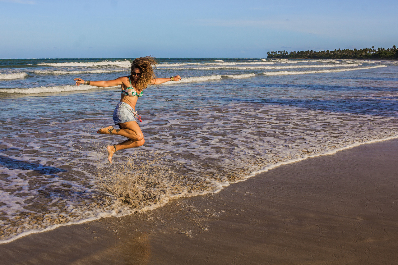 Mulher pulando na água durante ensaio feminino em Bainema, na Ilha de Boipeba, aproveitando o mar e a paisagem natural da Bahia.