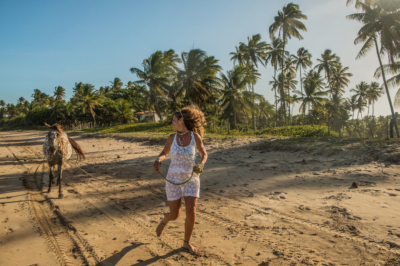 Mulher caminhando com um cavalo na praia de Bainema durante ensaio fotográfico feminino em Boipeba, cercada pela natureza preservada da Bahia.