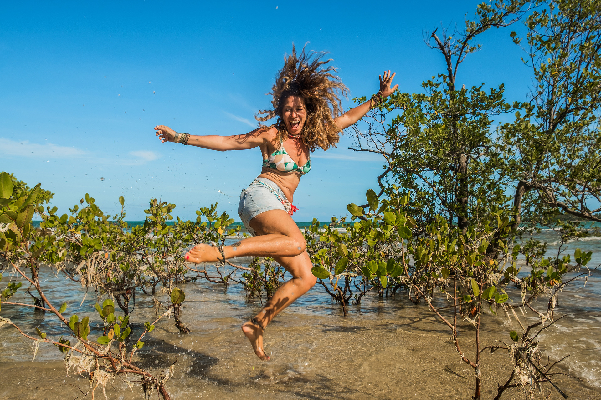 Mulher sorrindo e pulando durante ensaio fotográfico feminino na praia