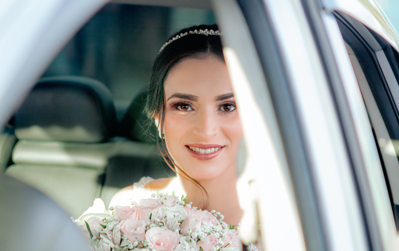 Foto da noiva dentro do carro, olhando para o a câmera e segurando o buquê antes de descer para a entrada na igreja.