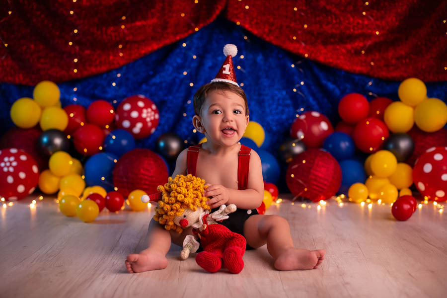 Cake ensaio bebe 1 ano tema palhacinho com bebe com maos em um bolo em formato de palhaco em cenario com tenda e baloes