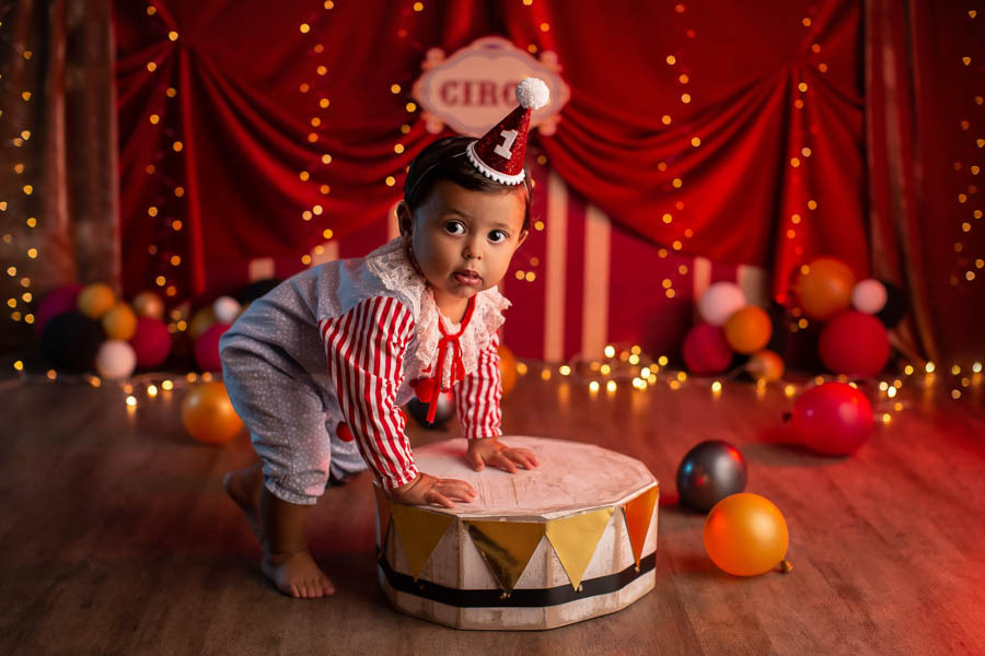 Ensaio 1 ano tema palhacinho com bebe com maos em picadeiro em cenario com tenda e baloes