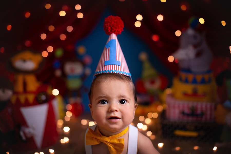 Smash the Cake ensaio bebe 1 ano tema palhacinho com bebe com maos em um bolo em formato de palhaco em cenario com tenda e baloes