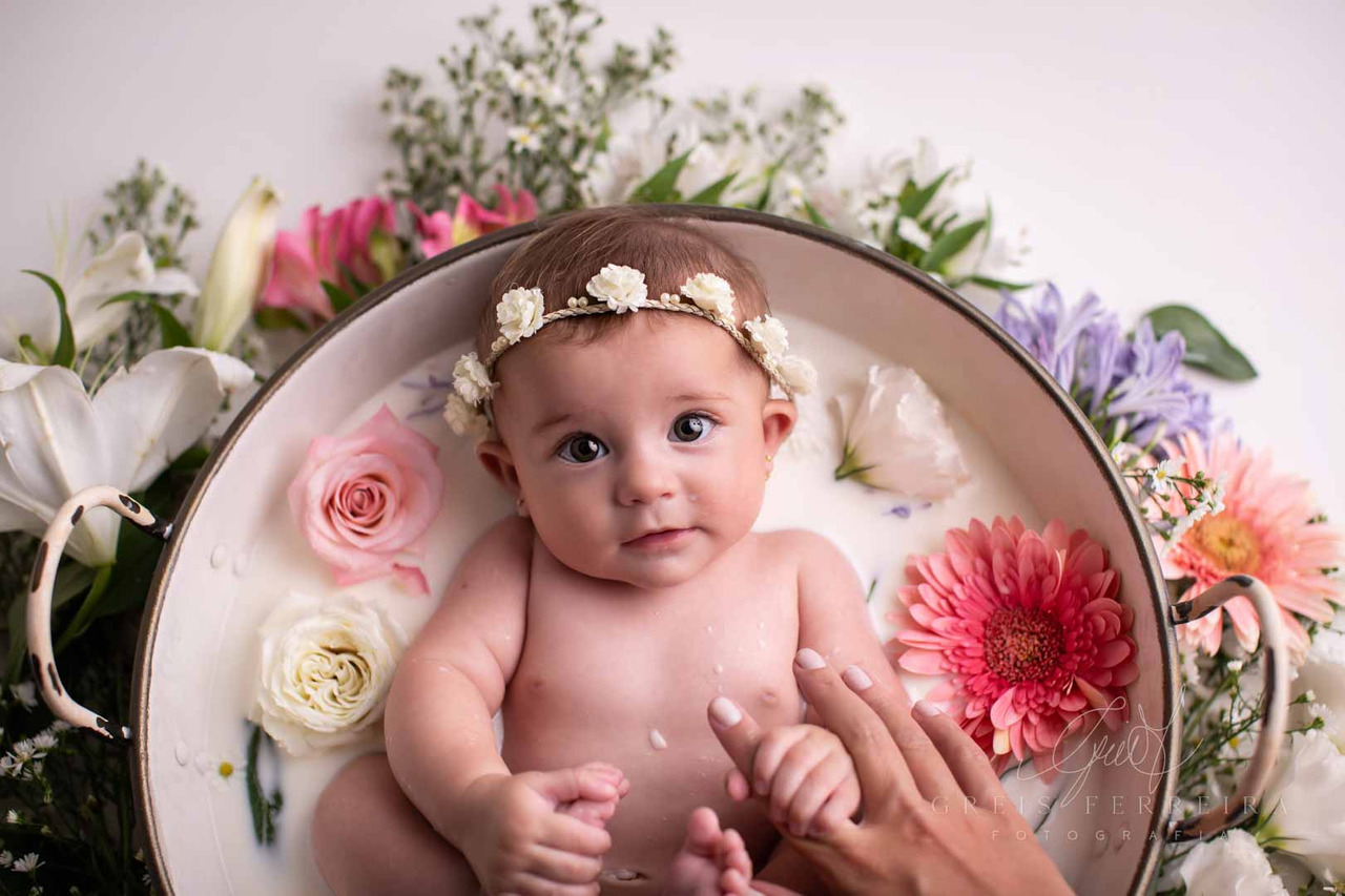 Bebê 4 meses usando tiara tomando banho de leite tina branca com flores ao redor