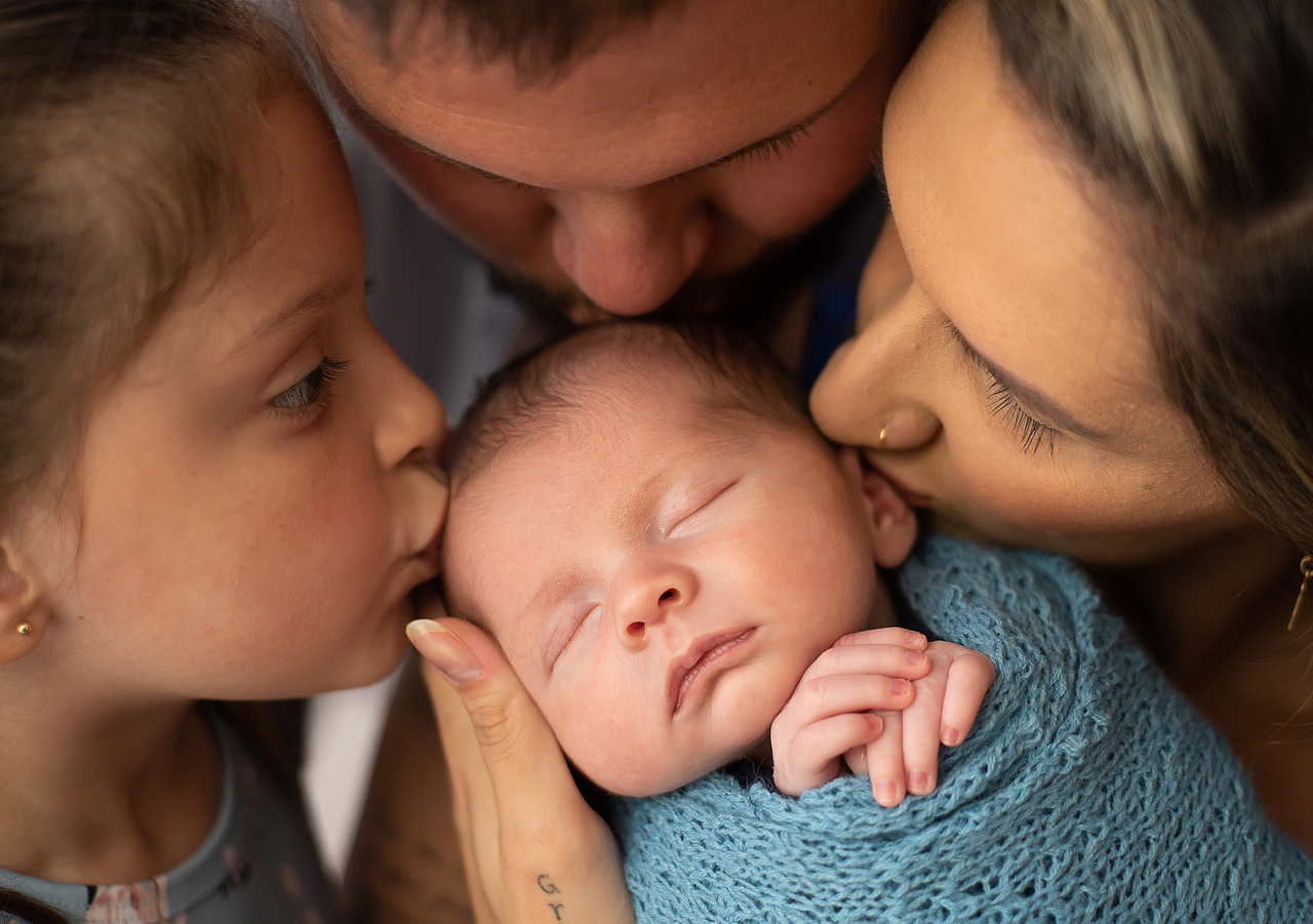 Família beijando um recém nascido foto de recem nascido que está sendo fotografado pela Aline fonte no estúdio de Bento Gonçalves em uma sessão de fotos newborn
