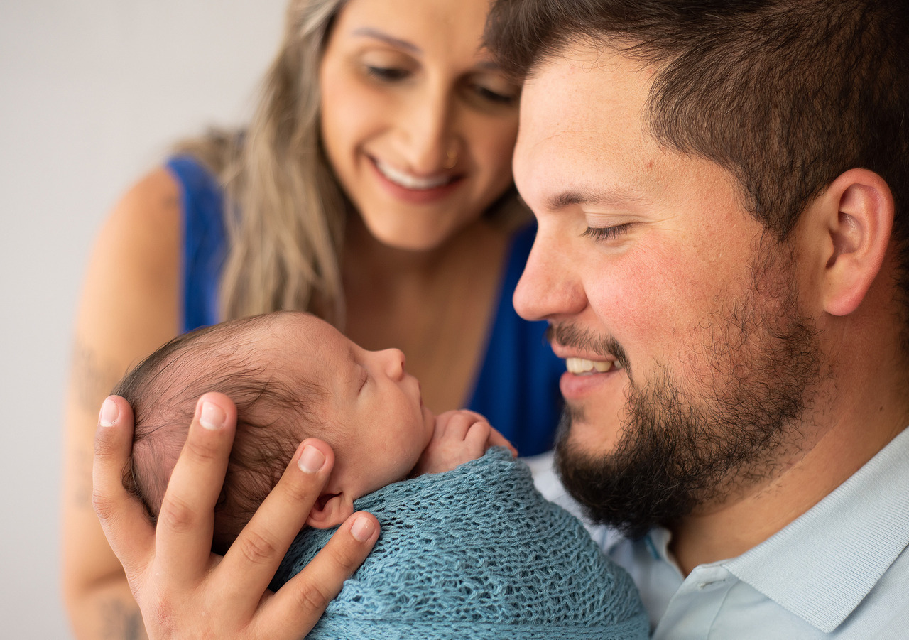 Sessão de fotos newborn onde o pai olha para o beber admirado pela linda pose que a fotógrafa Aline Fontes arrumou o bebê recém nascido em Bento Gonçalves