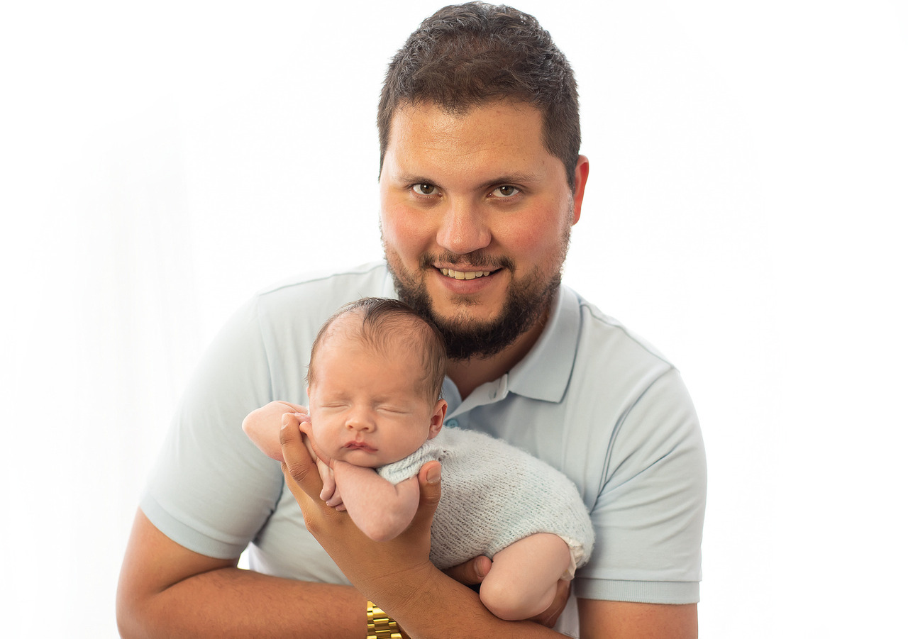 Pai segurando um bebê recém-nascido em uma pose de fotografia newborn feita pela Aline fone fotógrafo vice diretora da ABFRN