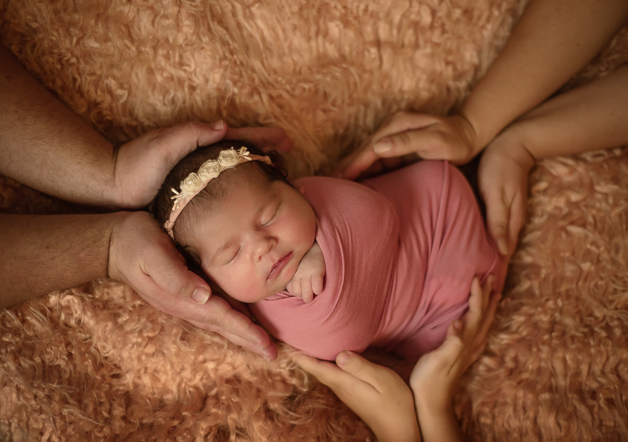 bebê enrolada em wrap rosa envolta das mãos da família