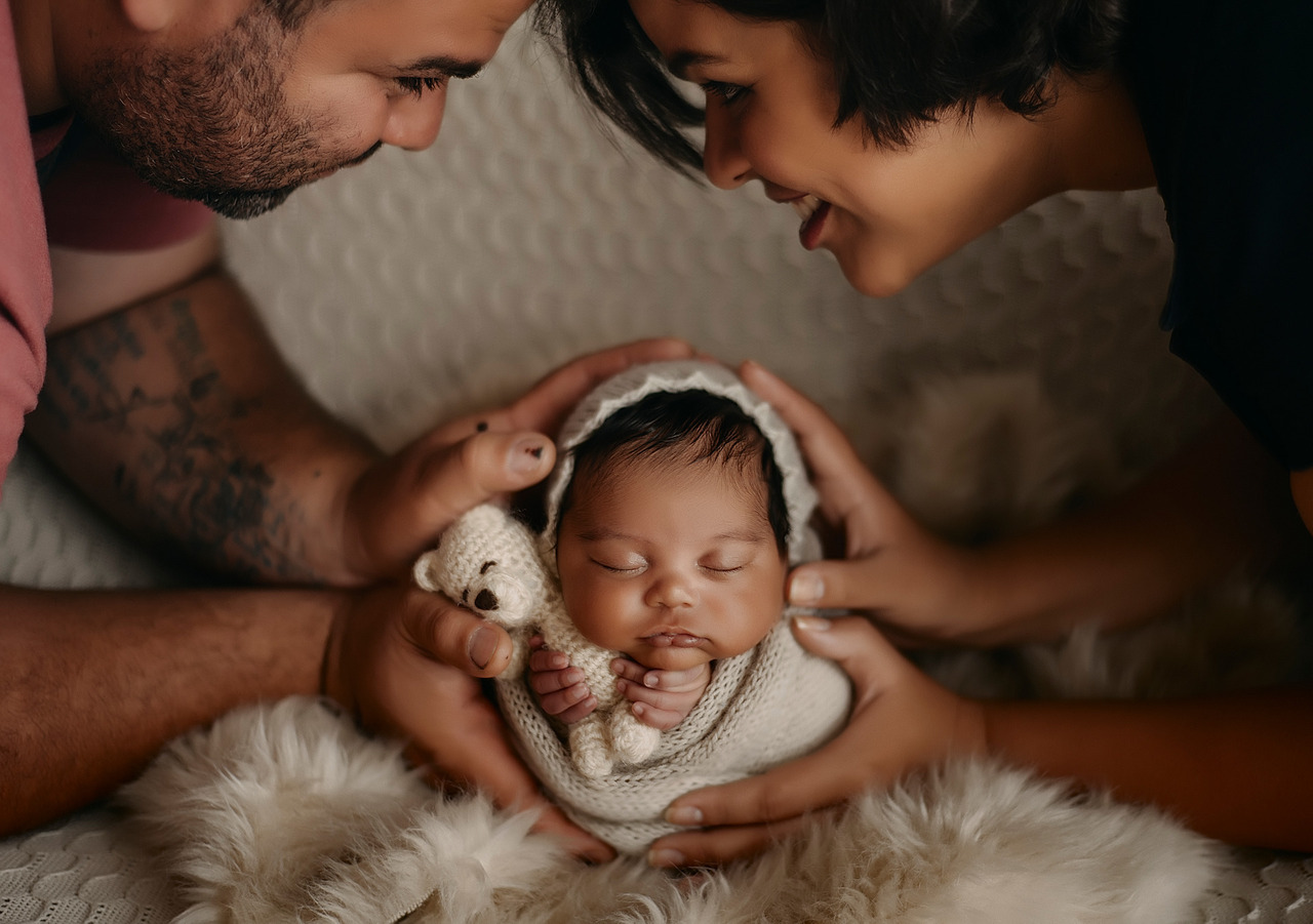 Pais com bebê recém-nascido nas mãos, bebê segurando ursinho