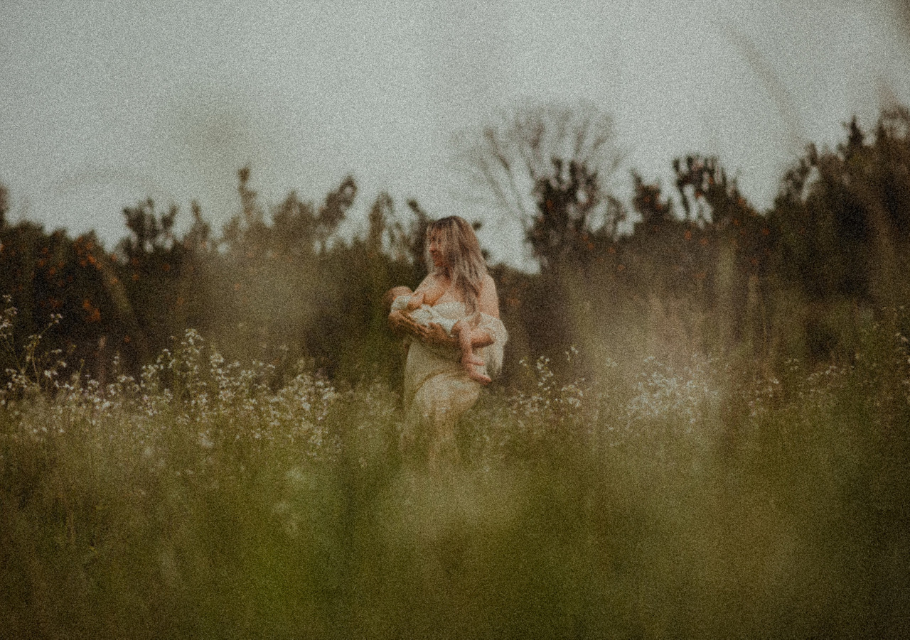 mulher amamentando bebê em campo de flores