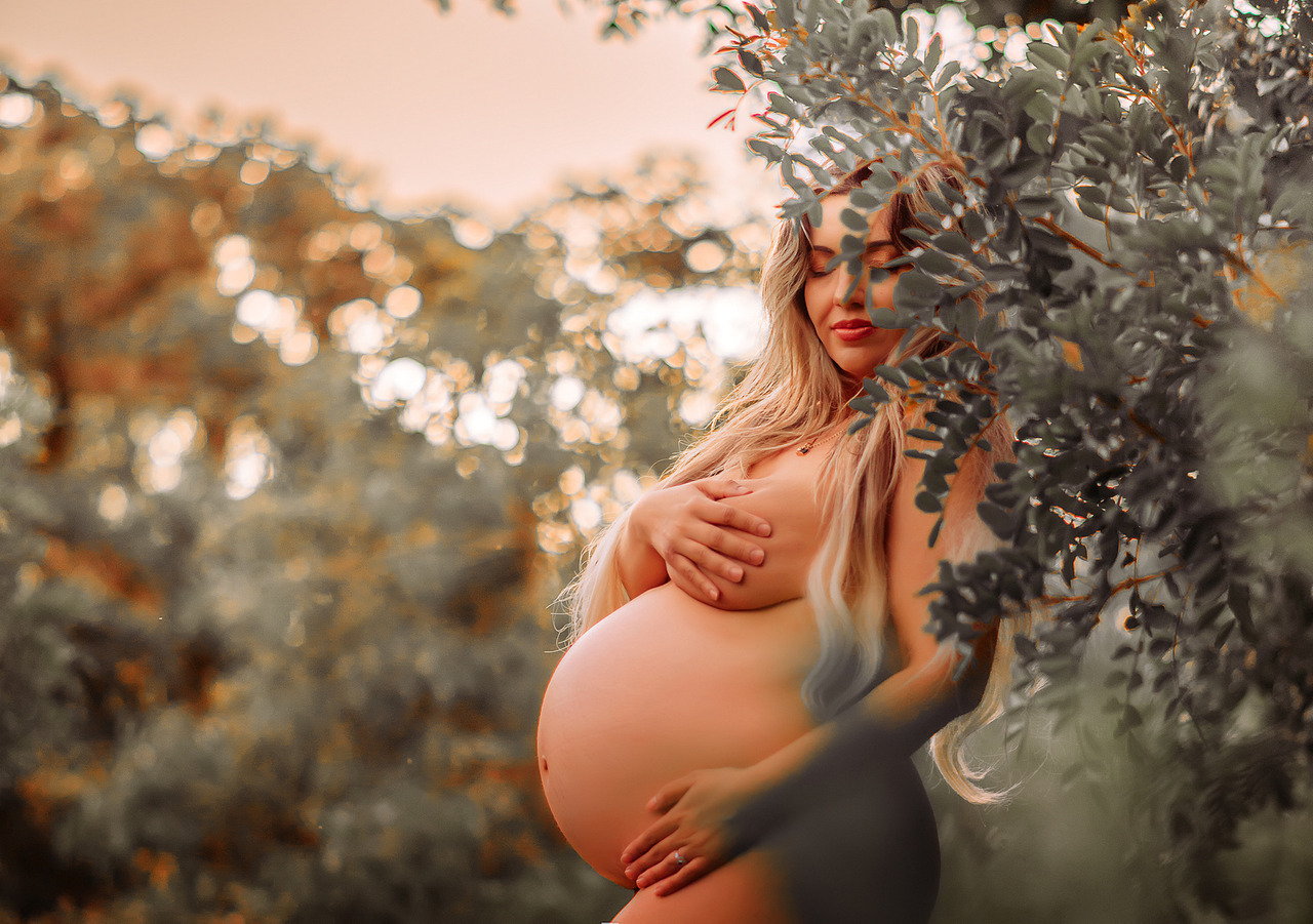 Mulher grávida em ensaio gestante artístico ao ar livre, envolta pela vegetação, com a barriga em evidência. A imagem retrata o corpo da mulher na gestação de forma natural, respeitosa e integrada ao ambiente, sem conotação sexual.