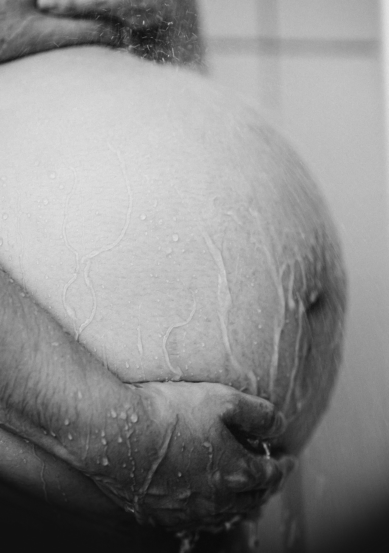 Detalhe em preto e branco da barriga de uma mulher grávida, evidenciando a pele, as marcas naturais da gestação e as mãos apoiadas sobre o ventre. Imagem que retrata a transformação do corpo da mulher durante a gestação de forma respeitosa e consciente.