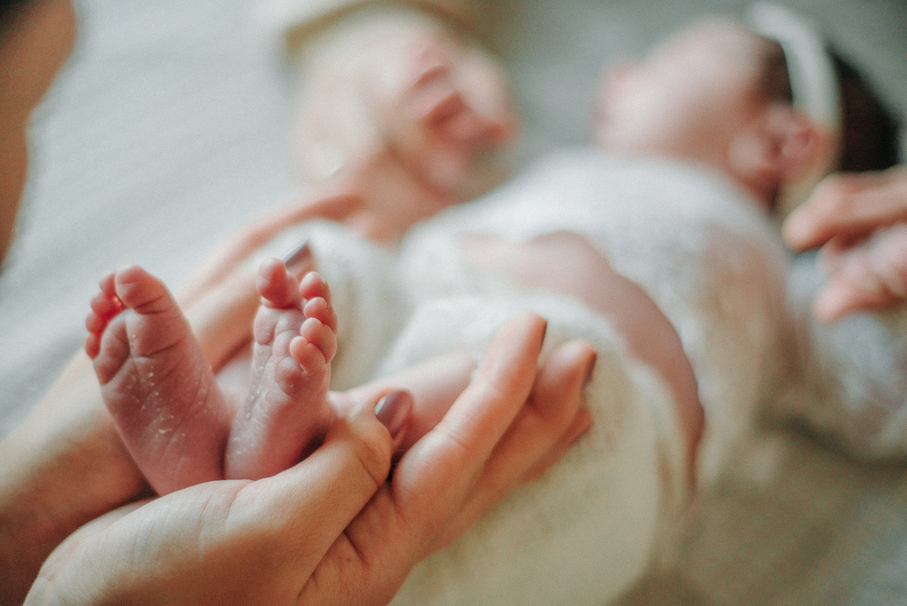 Detalhe dos pés de um bebê recém-nascido sendo segurados pelos pais durante ensaio newborn lifestyle com foco em vínculo, cuidado e fotografia infantil consciente.