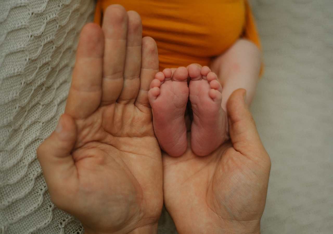 Detalhe dos pés de um bebê entre as mãos de um adulto, em guia da fotógrafa Aline Fontes para mães sobre fotos dos filhos nas redes sociais e imagem infantil.