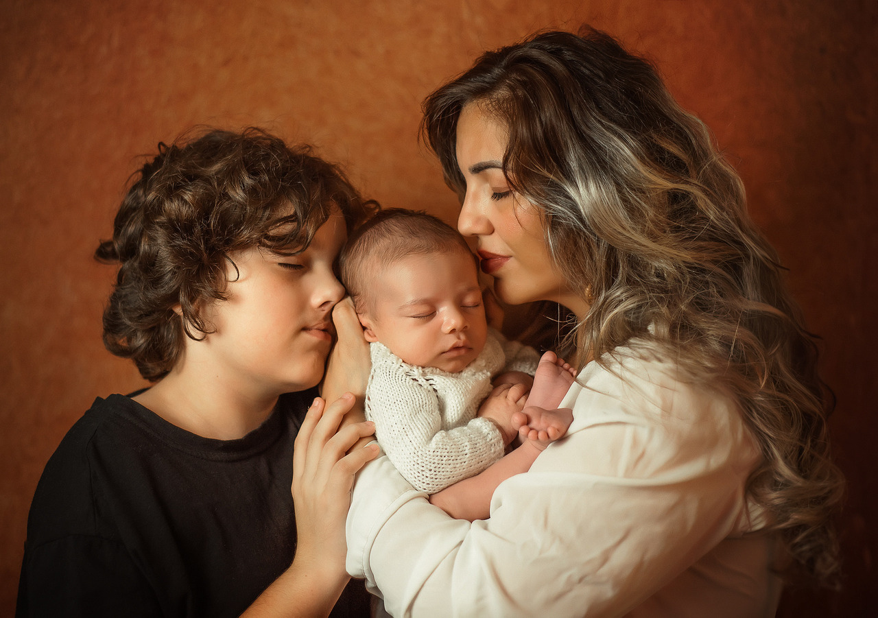 Mulher com dois filhos em retrato afetivo e intimista, com um bebê no colo e uma criança ao lado, em imagem que ilustra o guia criado pela fotógrafa Aline Fontes sobre compartilhamento consciente da infância e memória familiar.