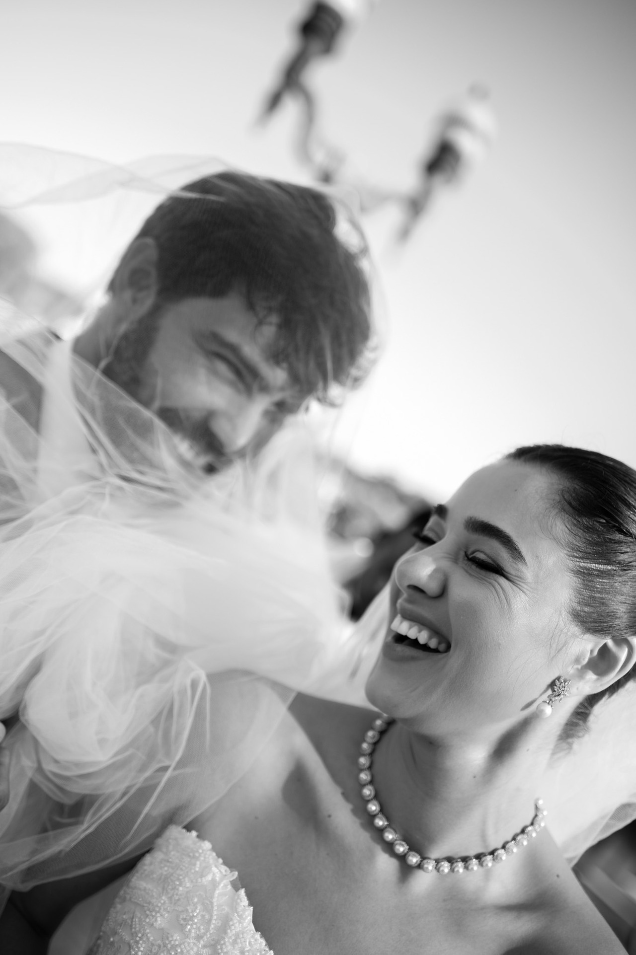 noivos trocam sorrisos espontaneos enquanto o véu da noiva cobre o rosto do noivo apos casamento