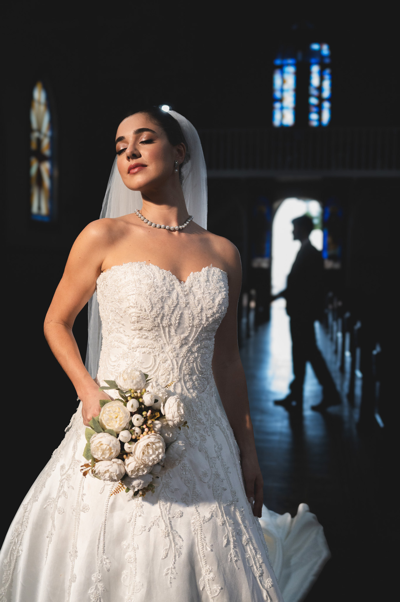 noiva posa com vestido marrie lafaiete enquanto silhueta do noivo e projetada ao fundo, fotografia de casamento com nivel elevado de beleza