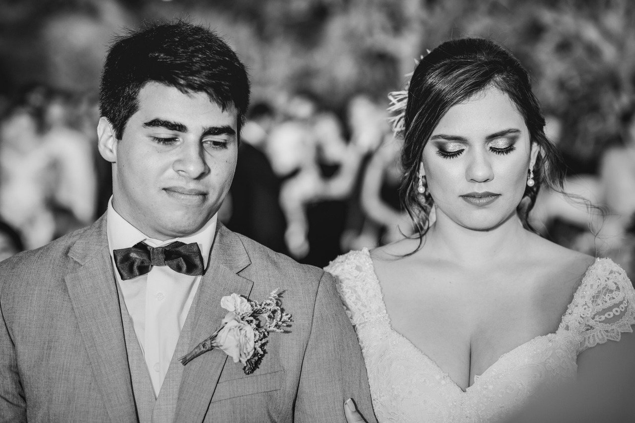 Casal de noivos lado a lado, de frente, em foto preto e branco. Noiva com vestido de decote coração.
