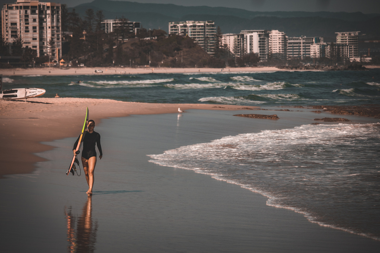 Garota caminhando em praia segurando uma prancha de surf