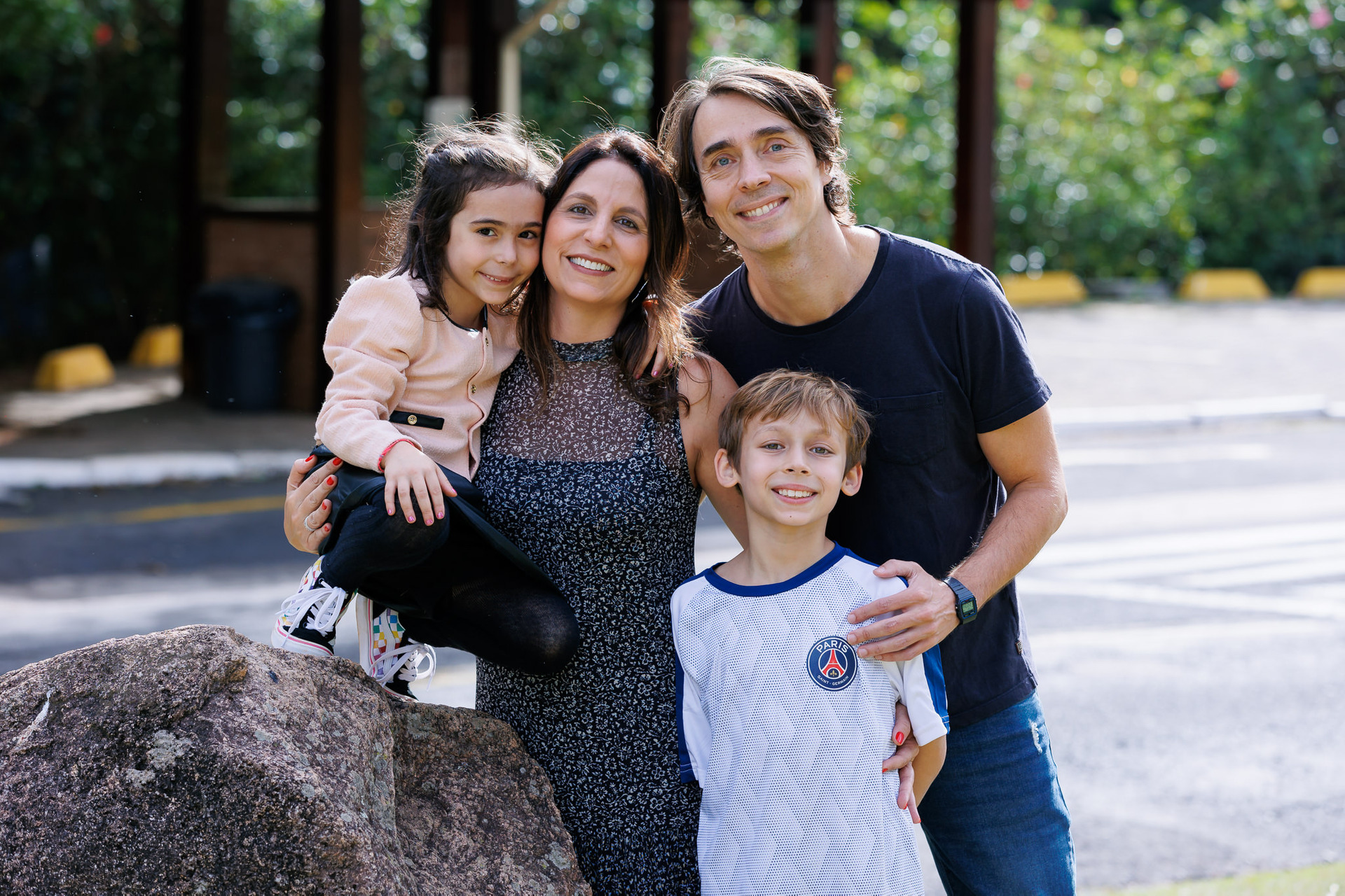 Retrato de família em aniversário infantil - pais e filhos abraçados em ambiente externo com luz natural