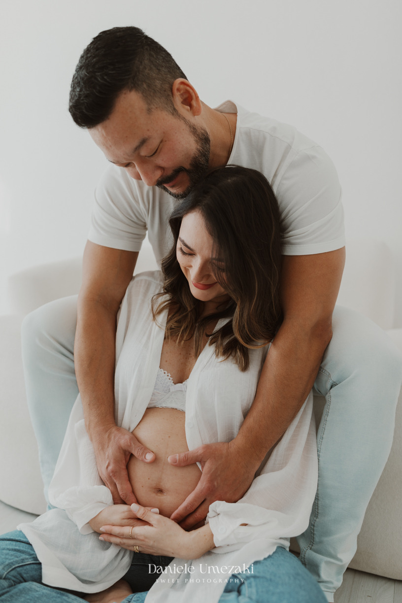 Casal abraçado durante ensaio gestante em Mogi das Cruzes, com foco nas mãos envolvendo a barriga em momento de carinho e conexão. Foto por Dani Umezaki Fotografia.