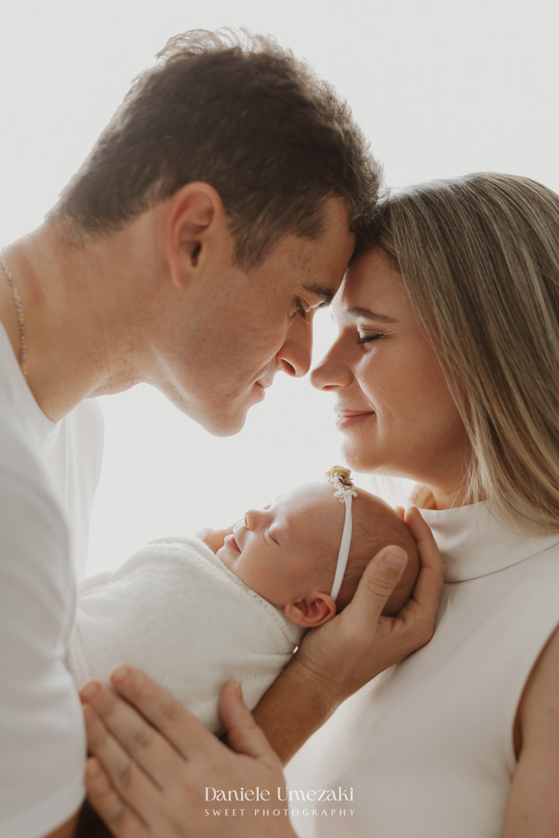 Pais observando a recém-nascida Pietra durante ensaio newborn natural realizado em estúdio em Mogi das Cruzes por Dani Umezaki, com fotografia leve, atemporal e cheia de afeto.