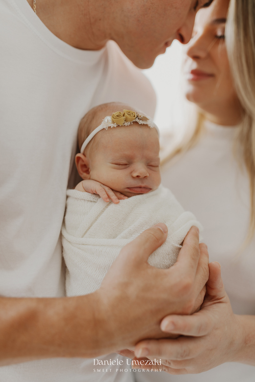 Pais segurando a recém-nascida Pietra durante ensaio newborn em estúdio em Mogi das Cruzes, registrando a conexão da família