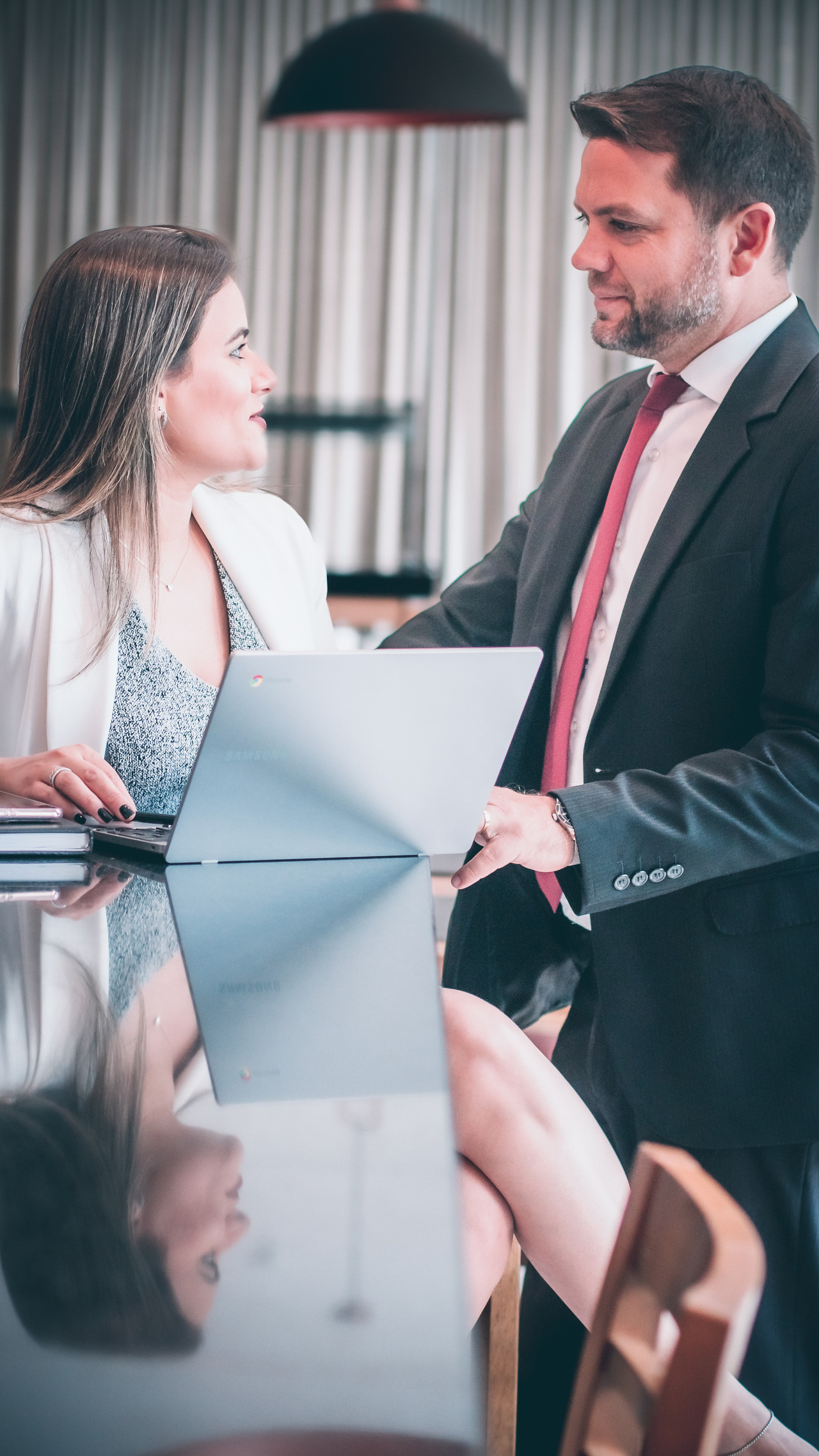Um casal trocando olhares num lounge de hotel enquanto compartilham algo na tela do notebook