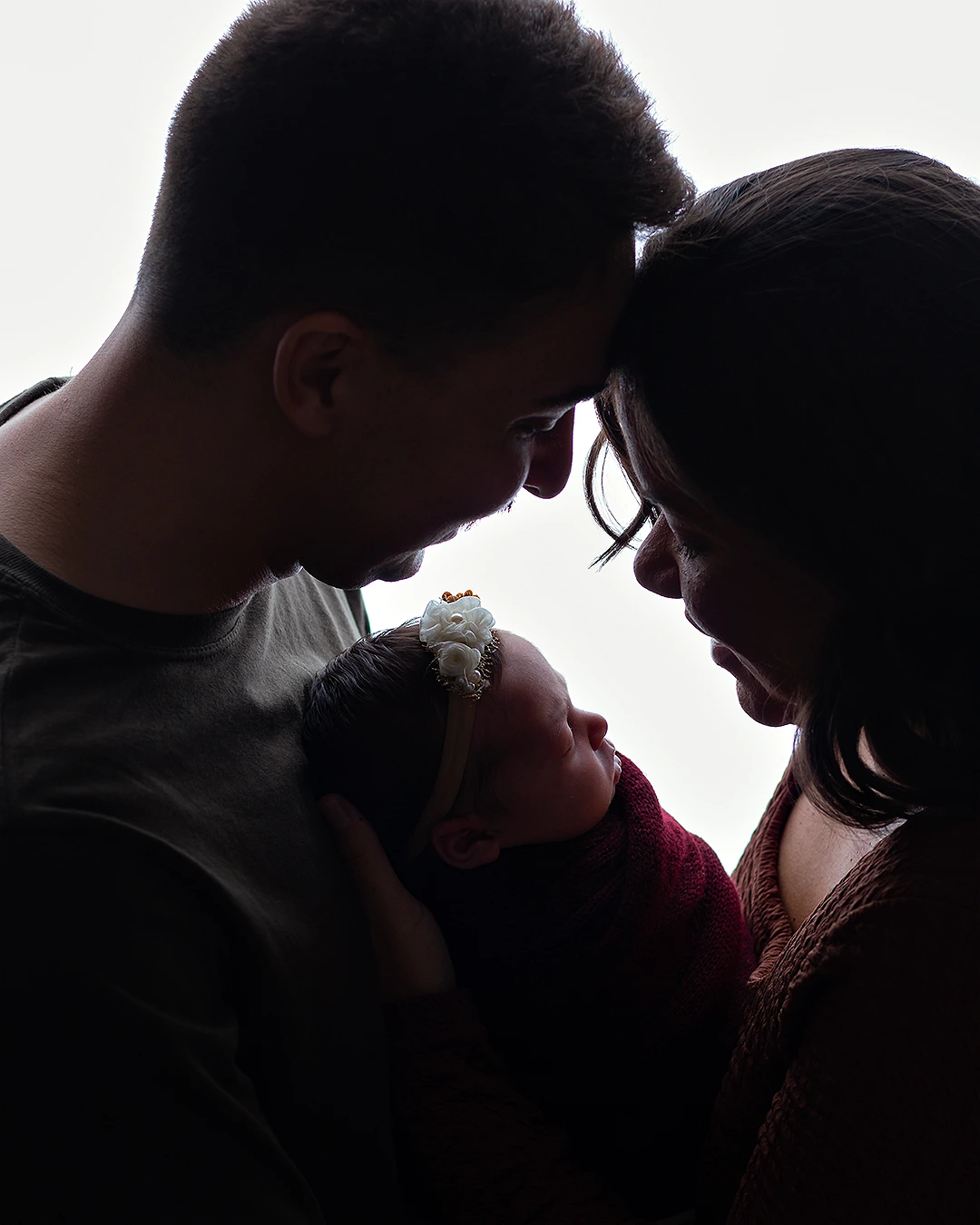 bebê nos braços do pai e da mãe. Foto contraluz, mostrando silhueta dos 3.