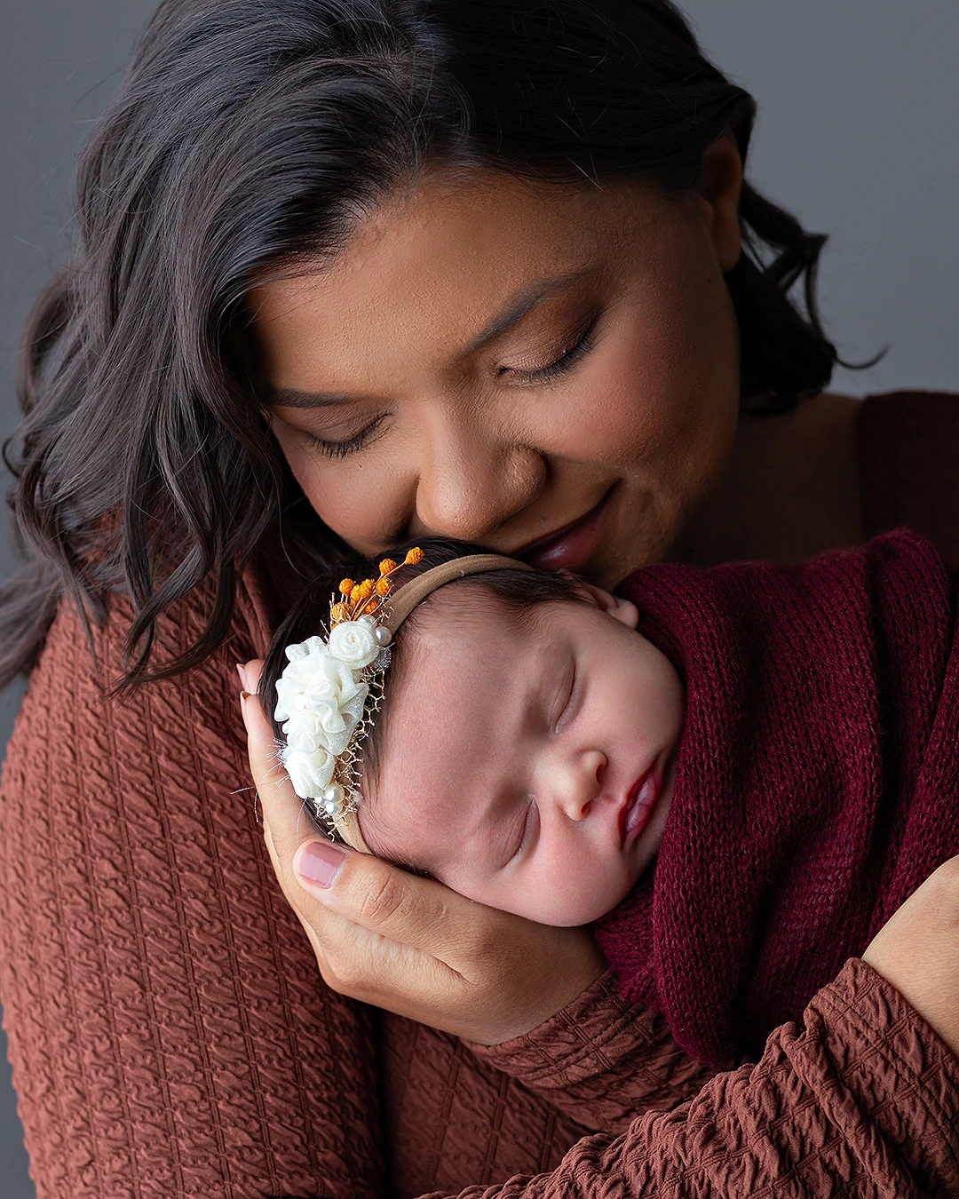 bebê recém-nascida enrolada em tecido feito casulo nos braços da mãe em ensaio Newborn.