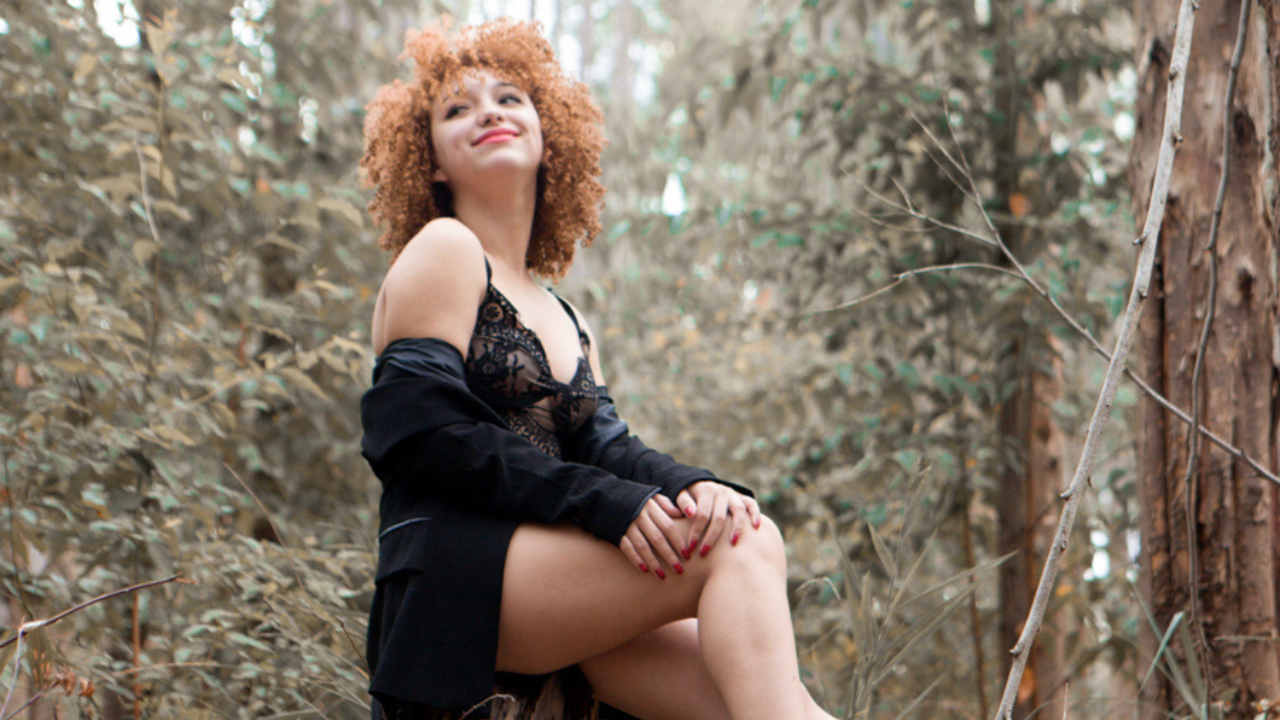 Mulher sentada em um toco de arvore no meio da floresta olhando para a vegetação