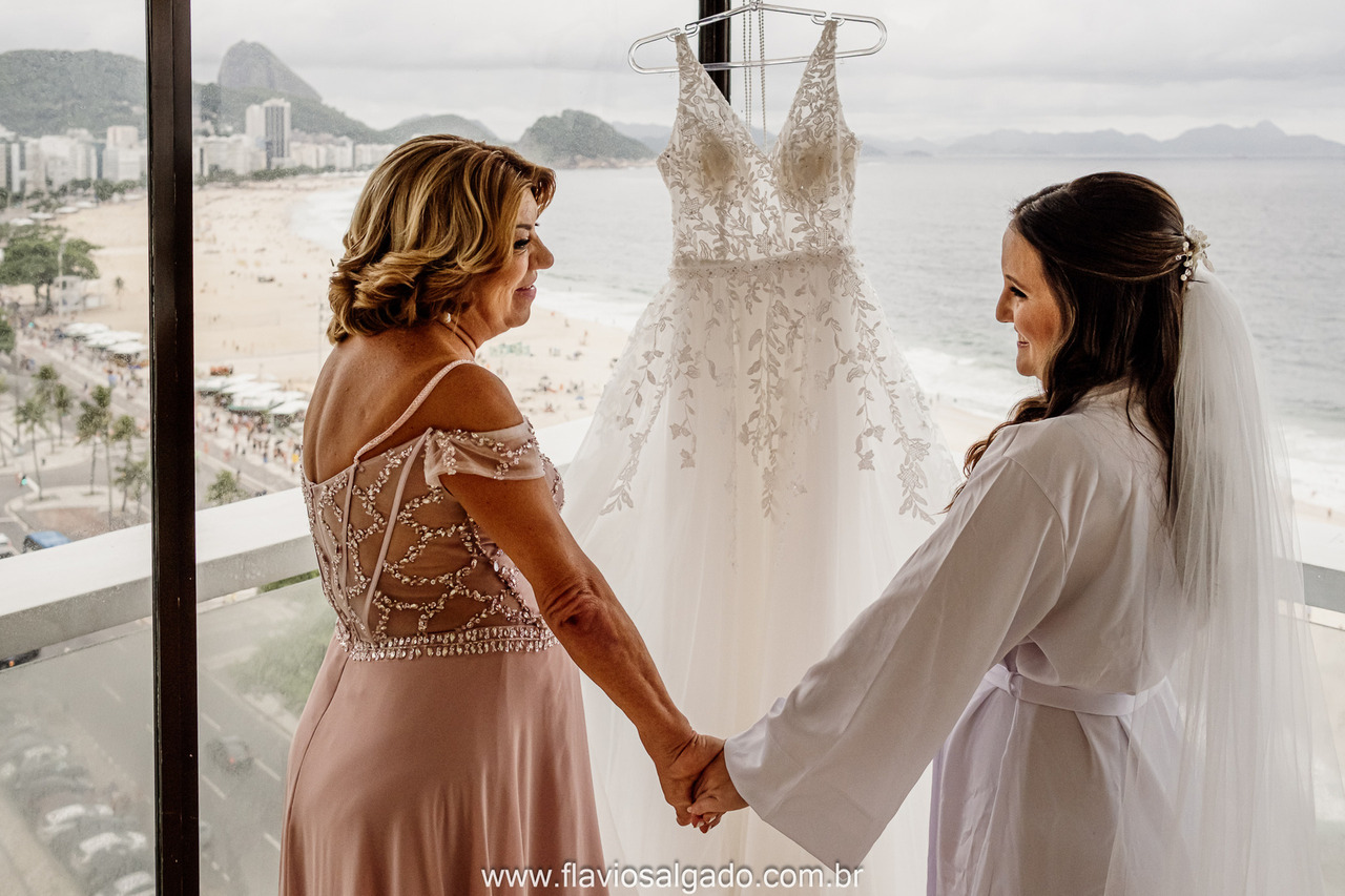 noiva e mãe dão as mãos de frente ao vestido com vista para o mar no rio de janeiro