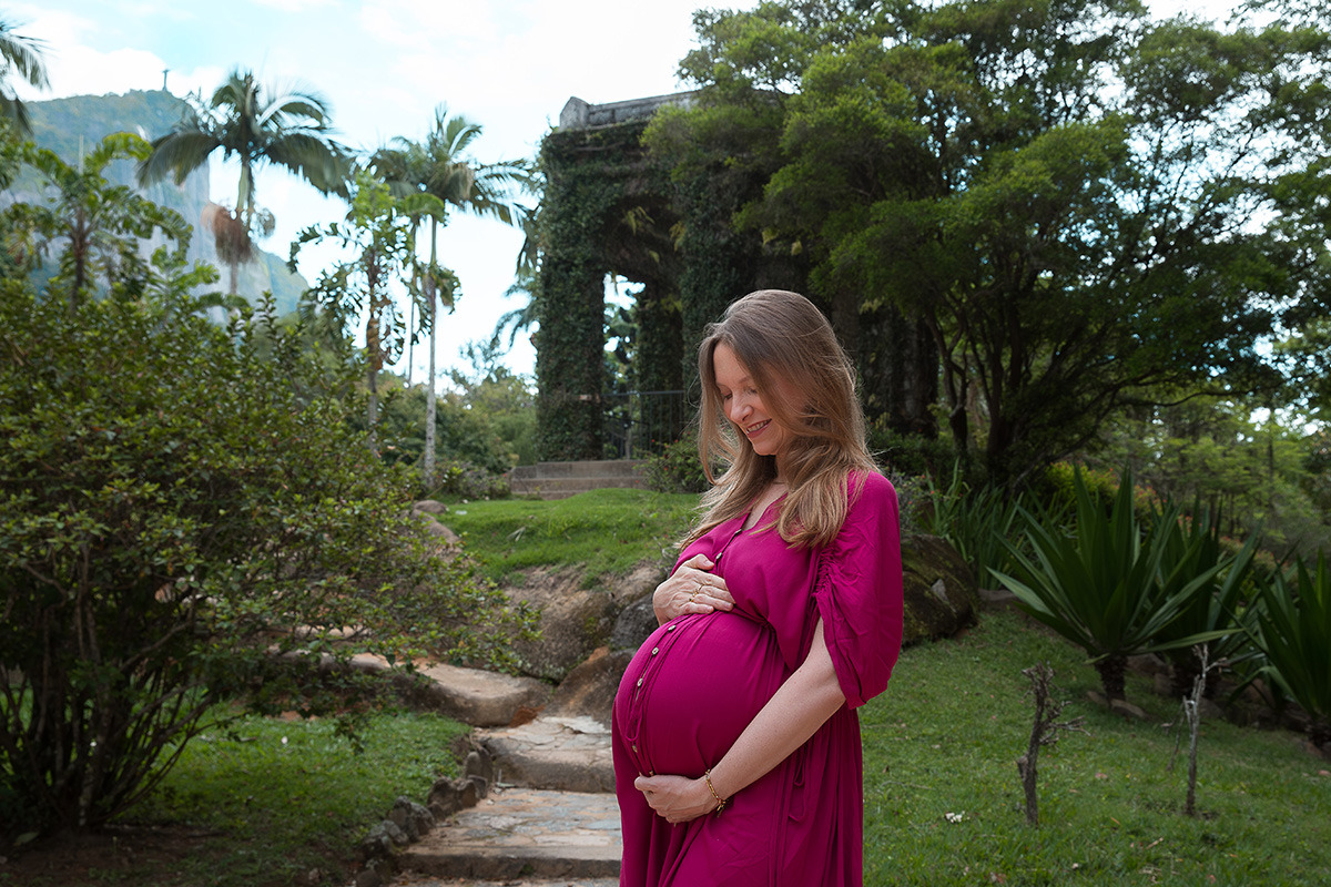 Gestante olhando barriga em frente a área arborizada no Jardim Botânico do Rio de Janeiro
