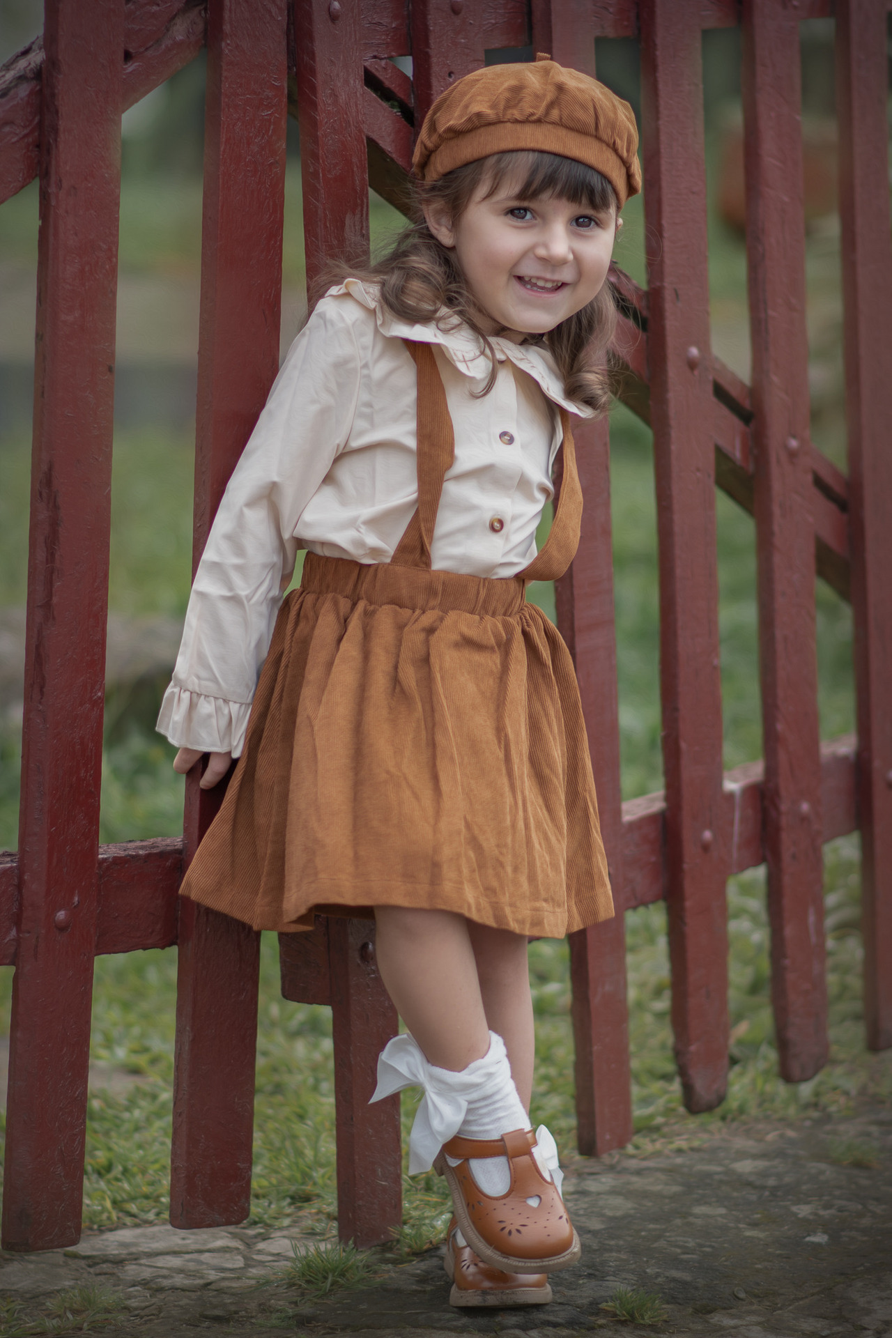 A foto mostra uma mãe sentada em um banco, com um vestido claro. Ela está segurando carinhosamente seus dois filhos pequenos. Um dos meninos está no colo dela, com um leve sorriso no rosto, enquanto o outro está de pé ao seu lado, também sorrindo. Ambos os meninos estão vestindo camisetas brancas e shorts claros, e estão descalços. A mãe e os filhos têm expressões de serenidade e carinho. Ao fundo, a grama e o ambiente natural criam um cenário calmo e bucólico, com uma luz suave que sugere que a foto foi tirada ao entardecer ou no início da manhã.