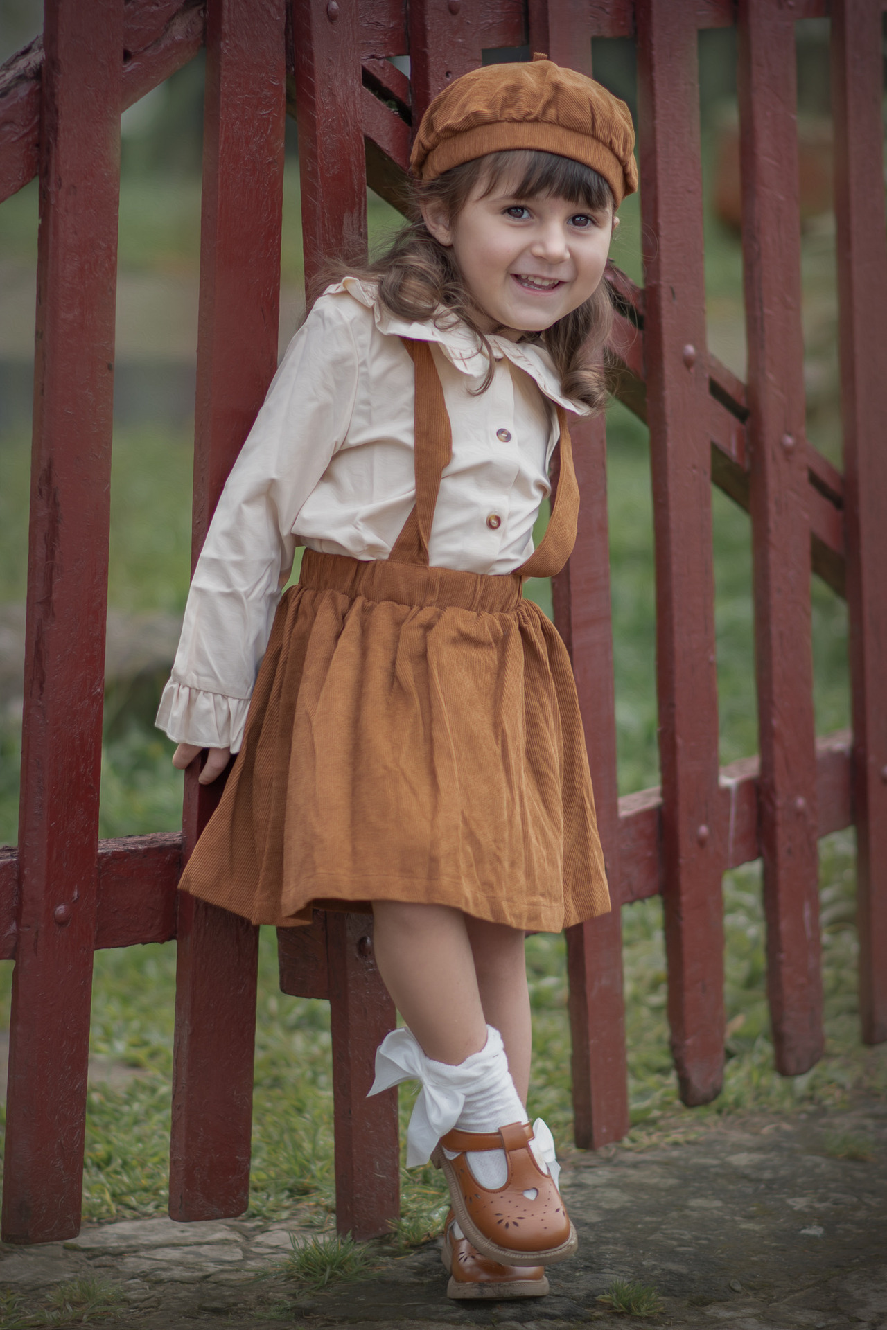 A foto mostra uma mãe sentada em um banco, com um vestido claro. Ela está segurando carinhosamente seus dois filhos pequenos. Um dos meninos está no colo dela, com um leve sorriso no rosto, enquanto o outro está de pé ao seu lado, também sorrindo. Ambos os meninos estão vestindo camisetas brancas e shorts claros, e estão descalços. A mãe e os filhos têm expressões de serenidade e carinho. Ao fundo, a grama e o ambiente natural criam um cenário calmo e bucólico, com uma luz suave que sugere que a foto foi tirada ao entardecer ou no início da manhã.