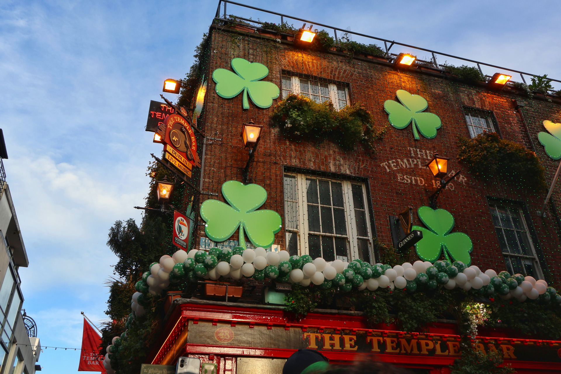 Fotografia de um pub irlandês em pleno St. Patrick's Day, com iluminação verde vibrante, pessoas brindando e música ao vivo, capturada por ex-aluno do curso, demonstrando a aplicação das técnicas de fotografia manual para registrar a vivacidade e a atmosfera autêntica da celebração.
