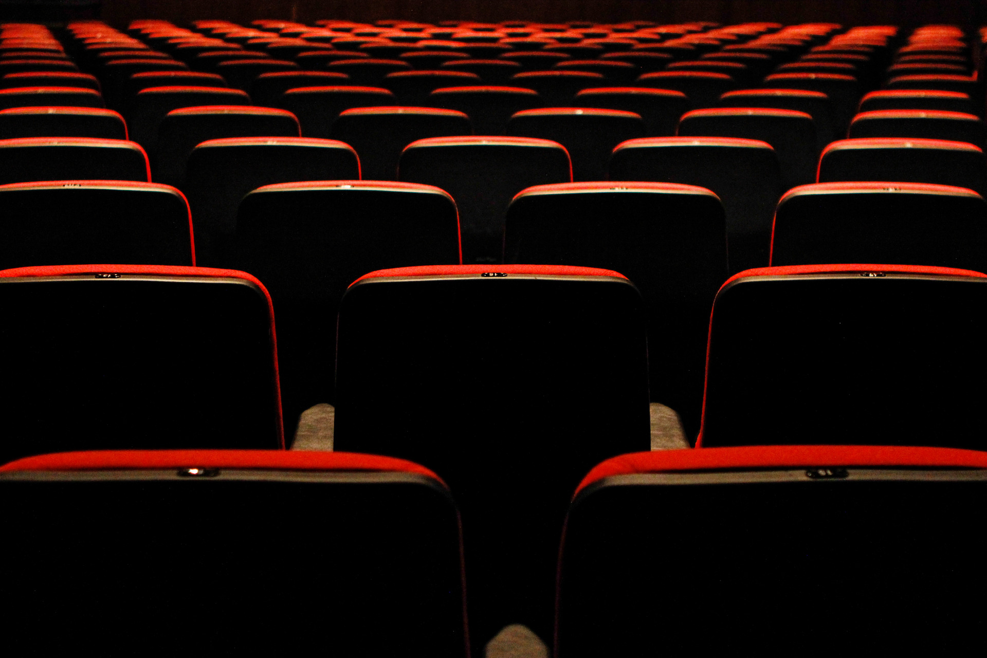 Fotografia de bancos de teatro vermelhos dispostos em sequência geométrica, destacando as linhas e a textura do estofamento, ideal para projetos de design ou arquitetura.