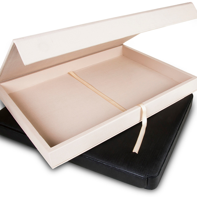 Estojo de álbum profissional na cor marfim, aberto para revelar uma fita interna que facilita a remoção do álbum. O estojo possui fecho magnético e está posicionado sobre um estojo preto, demonstrando o acabamento premium.