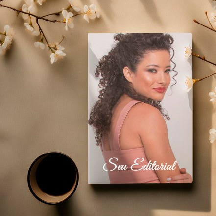 Álbum fotográfico posicionado em uma mesa ao lado de um copo de café e galhos com flores, com a capa exibindo uma modelo em plano médio olhando por cima dos ombros, sugerindo um editorial elegante e intimista.