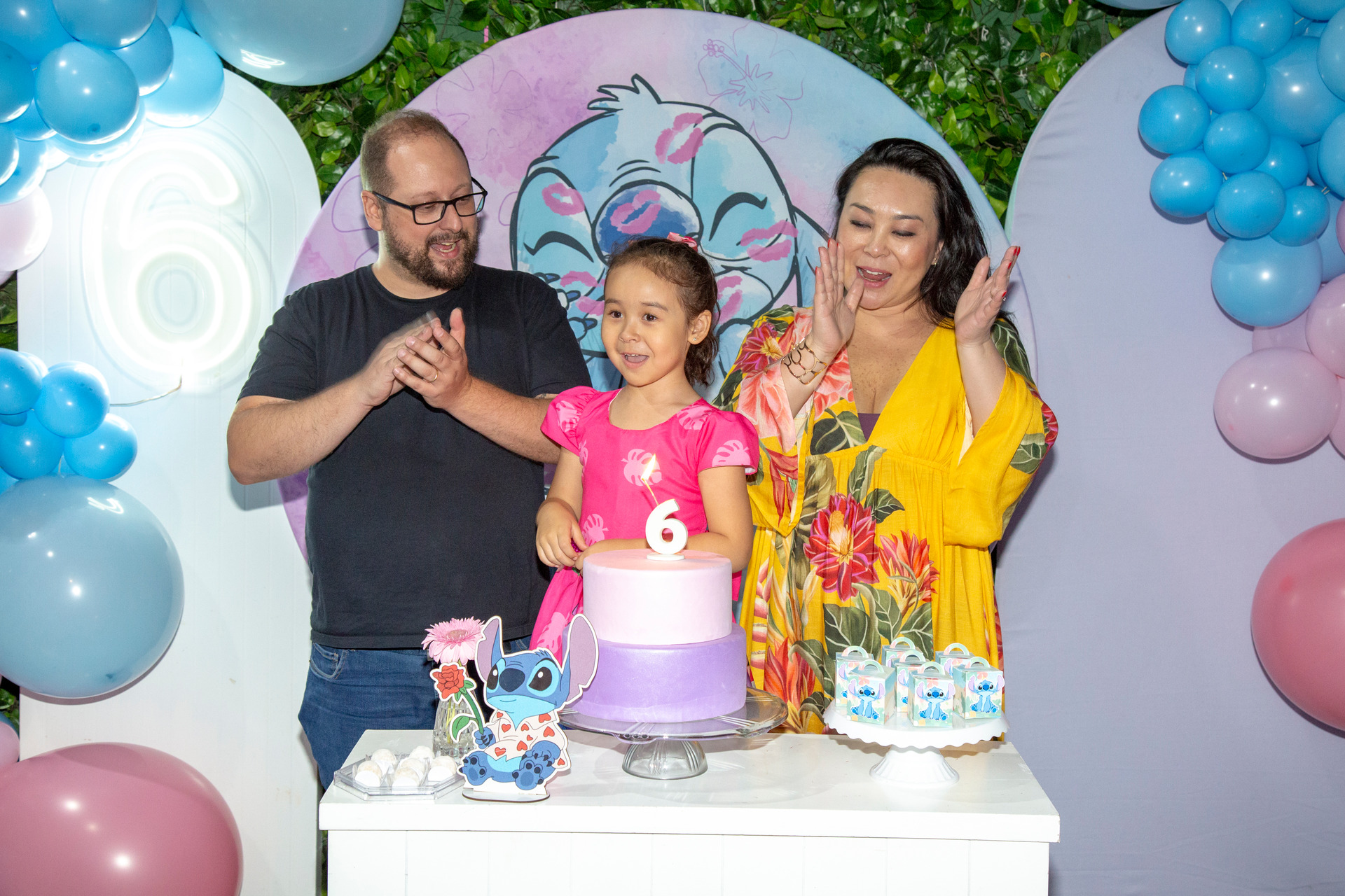 Pais cantando parabéns com carinho para a filha de 6 anos em um buffet infantil em São Paulo, com decoração temática de Lilo & Stitch, um momento emocionante de celebração de aniversário infantil em São Paulo e foto de Bruno Arita