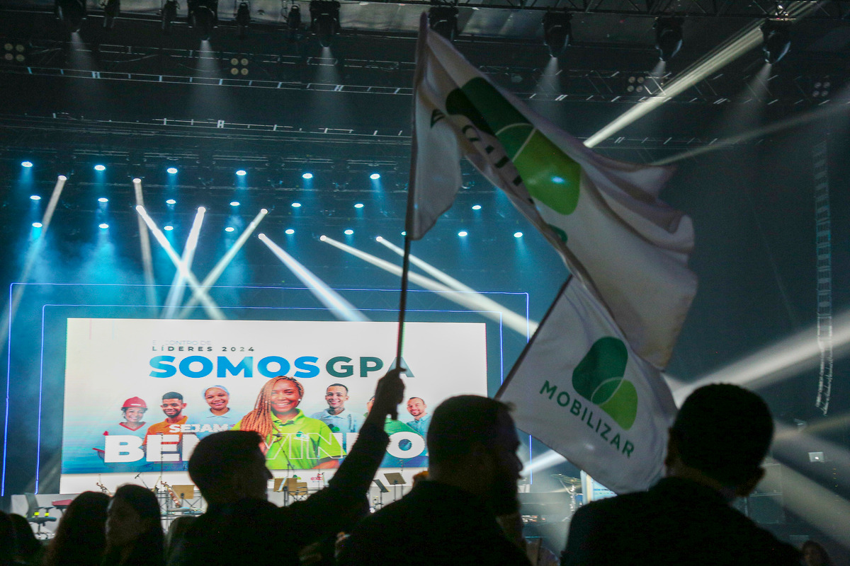 Grande evento para mil pessoas com palco ao fundo e silhueta de convidados em foto grandiosa de evento de Bruno Arita