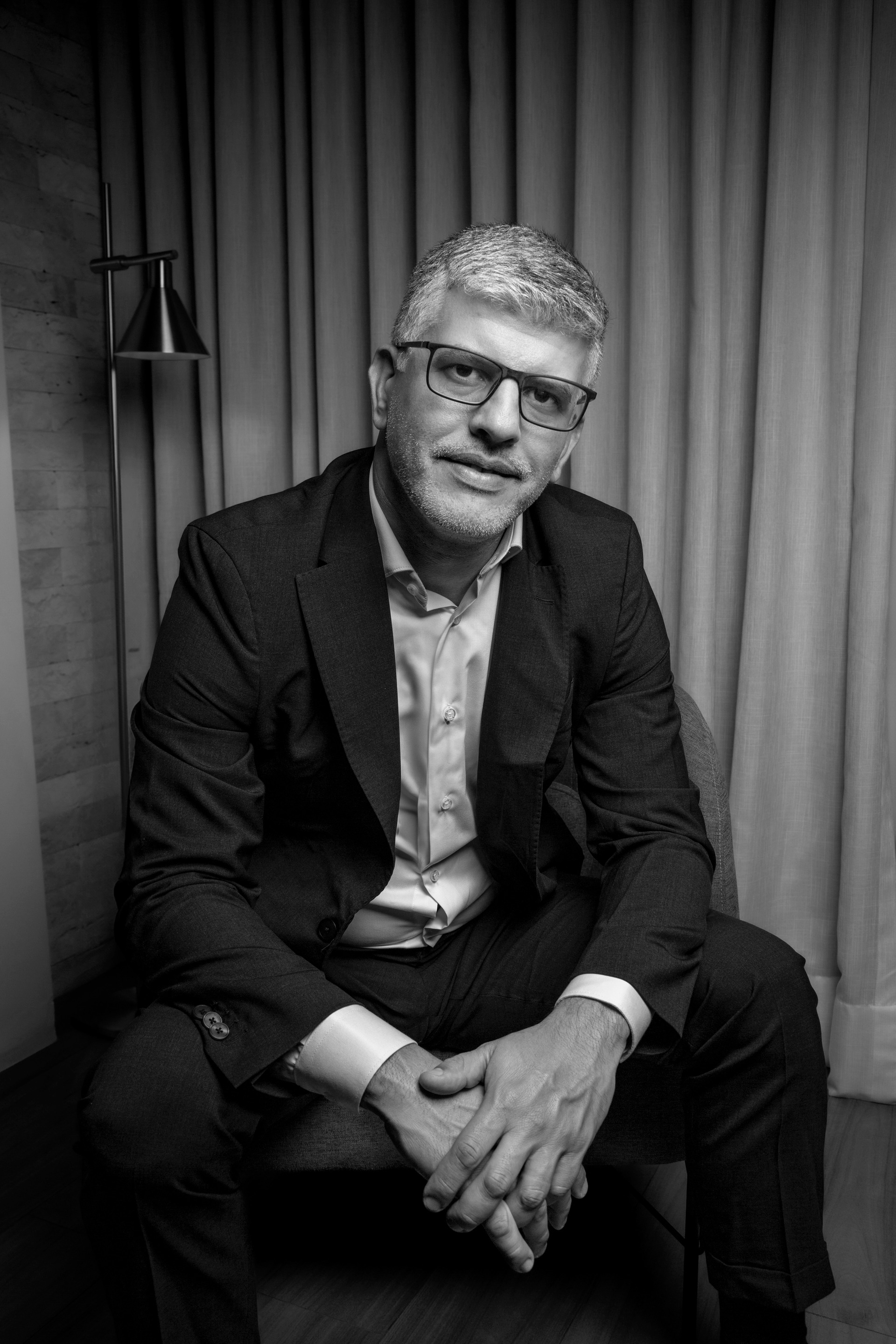 Retrato editorial de homem de meia idade sentado em pose elegante olhando com confiança em cenário elegante em imagem preto e branco por Bruno Arita