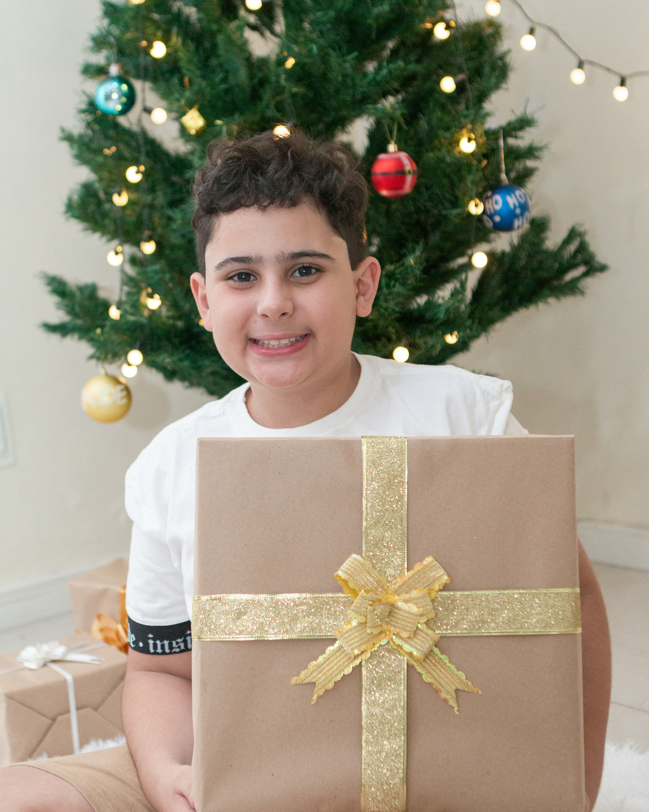 Menino com presente nas mãos e arvore de Natal ao fundo
