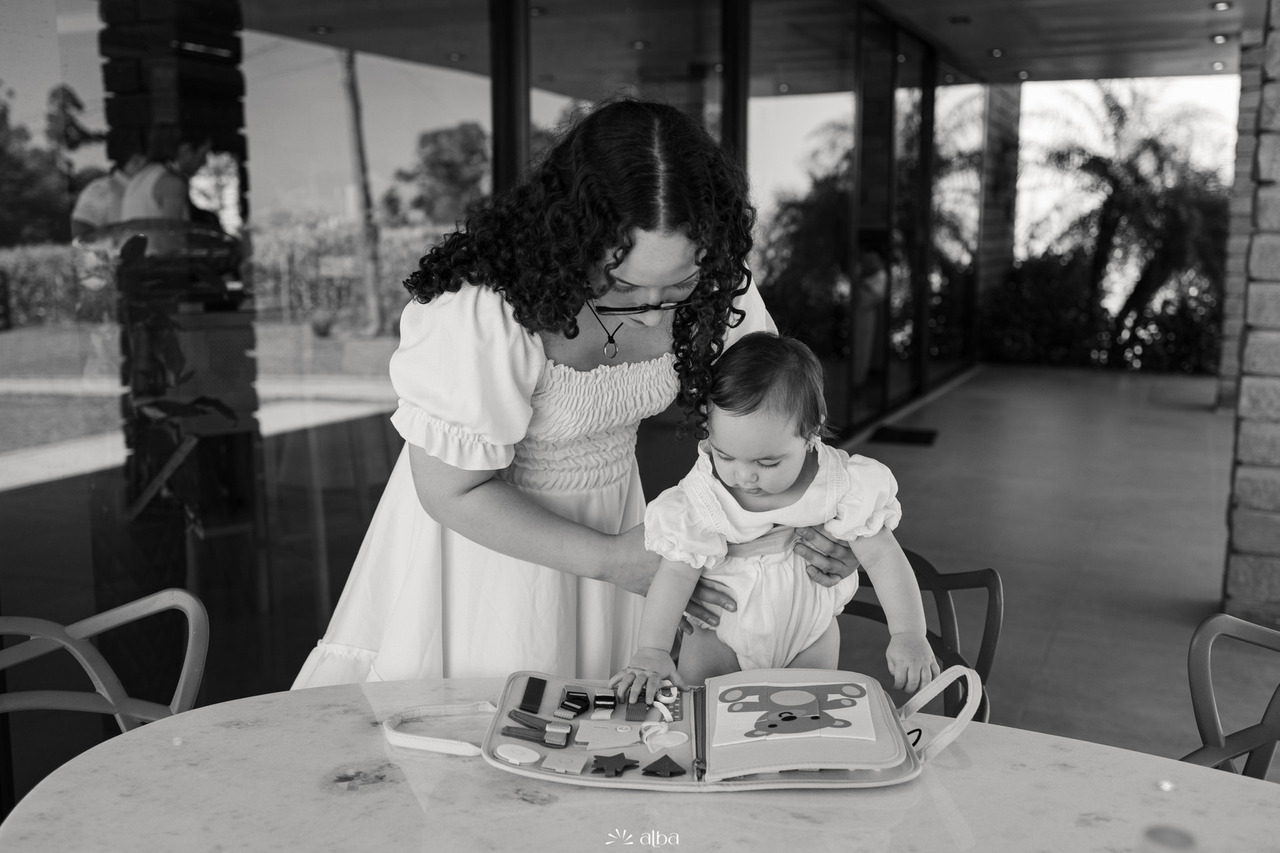 Familiar interage com a Amália durante a comemoração do batizado na casa da família, em Estrela, destacando momentos naturais da celebração. Foto: Alba Estúdio.