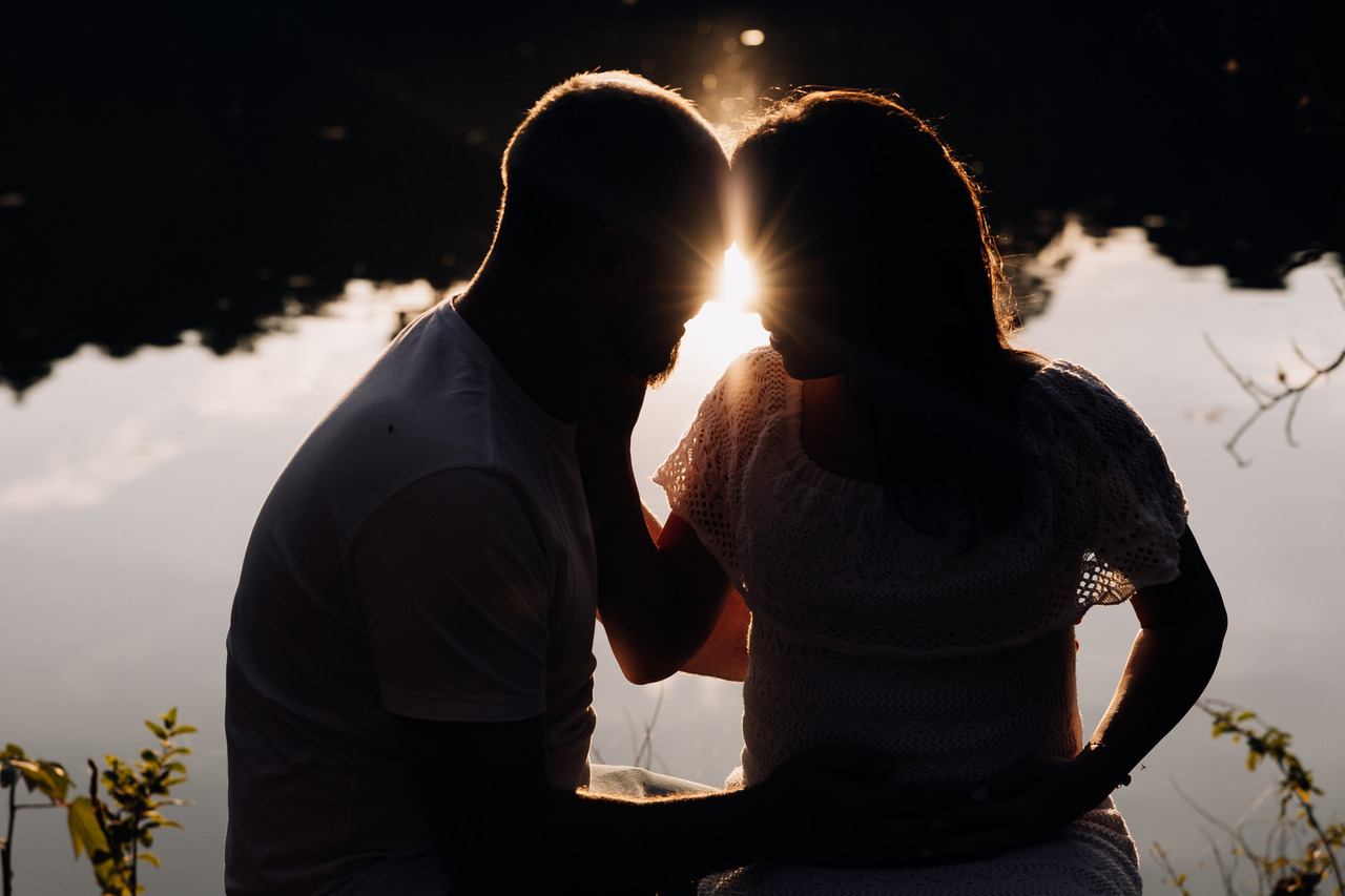 Casal em ensaio gestante externo ao pôr do sol com silhueta romântica refletida na água | Fotografia de gestante Alba Estúdio em Lajeado
