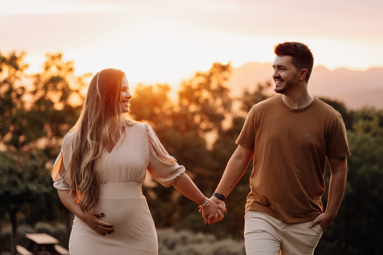 Casal caminhando de mãos dadas durante ensaio gestante externo ao pôr do sol | Fotos espontâneas de gestante em Lajeado - Alba Estúdio  Foto 3